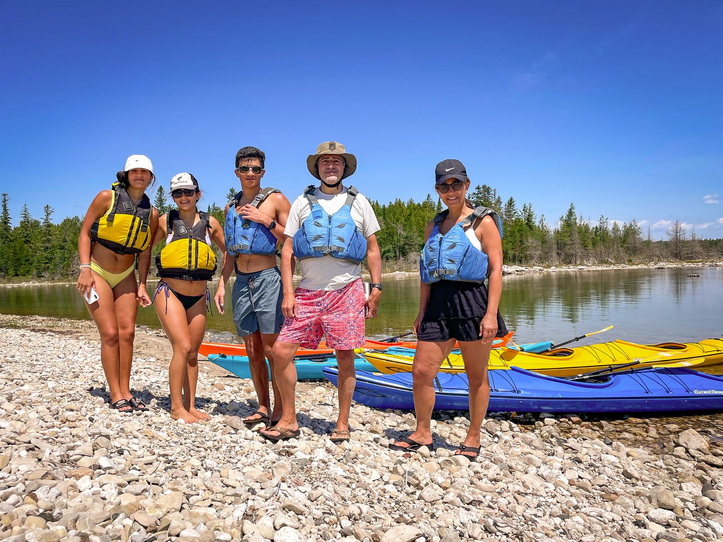 A family with three teenagers stands on a rocky shoreline taking a short break on Penny Island in the Les Cheneaux Islands during a Little Dipper kayak tour.