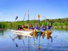 A group of kayaks raise their paddles into the air on a sunny summer day. Everyone is smiling.